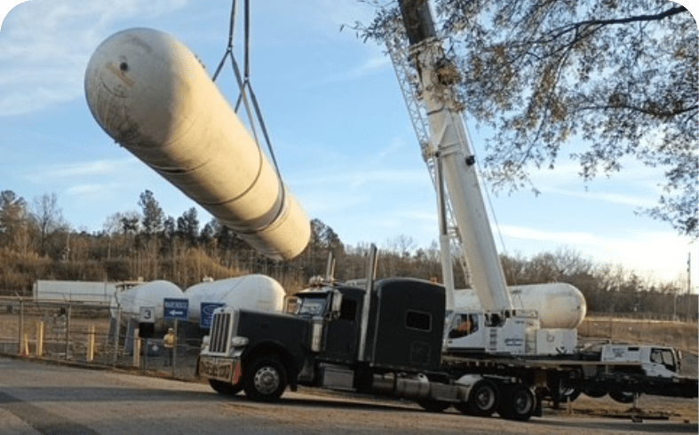A crane lifts a large cylindrical pipe onto a truck at a construction site.